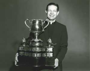 Black and white photo from the Basilian Archives. Fr. Bauer smiles and poses with a trophy.