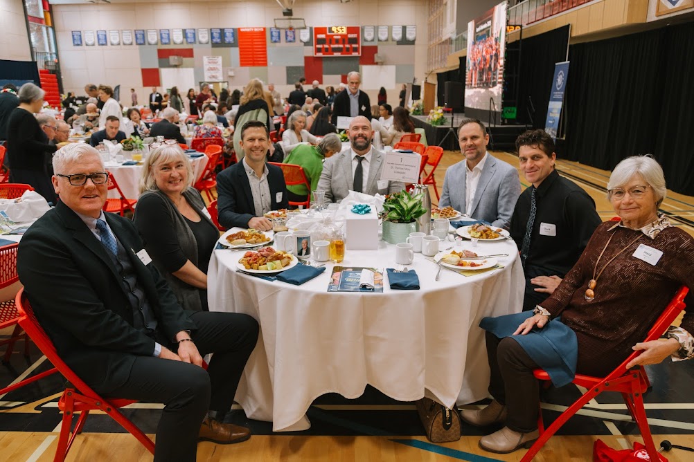 A table of guests and donors smiles for a photo at the 25th Annual Fundraising Breakfast for Corpus Christi College and St. Mark's College.