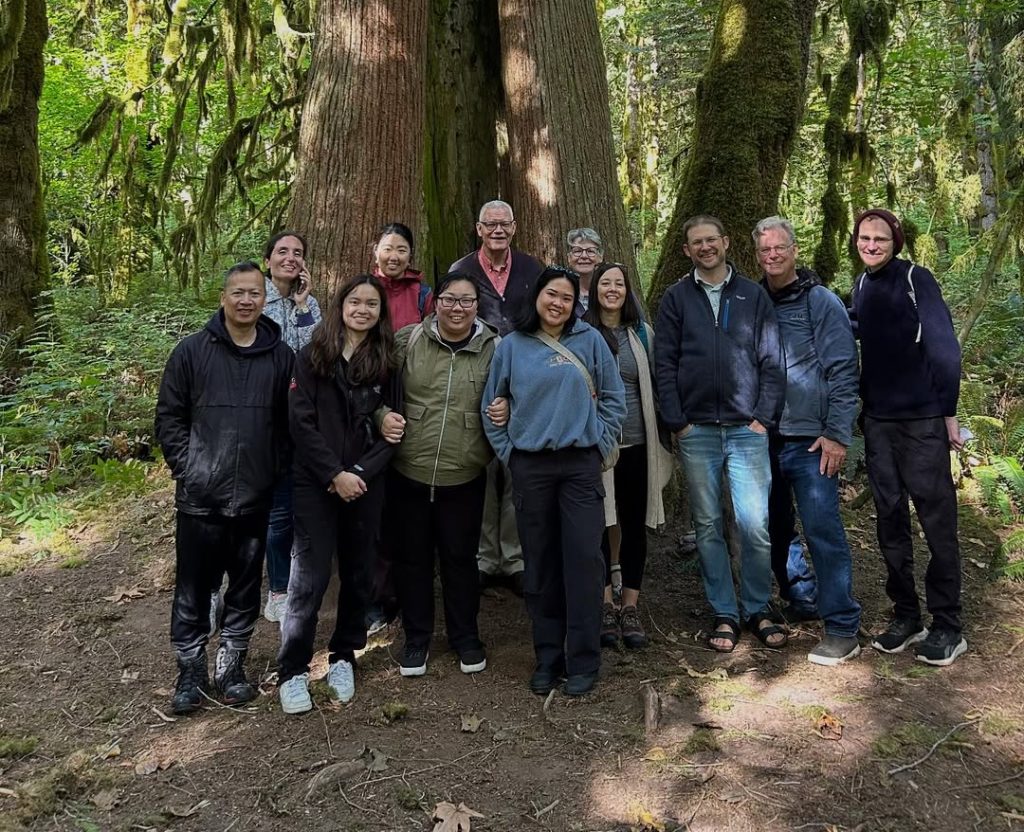 A group of St. Mark's faculty and staff smile for a photo in front of a large cedar tree at a retreat in Squamish Nation.